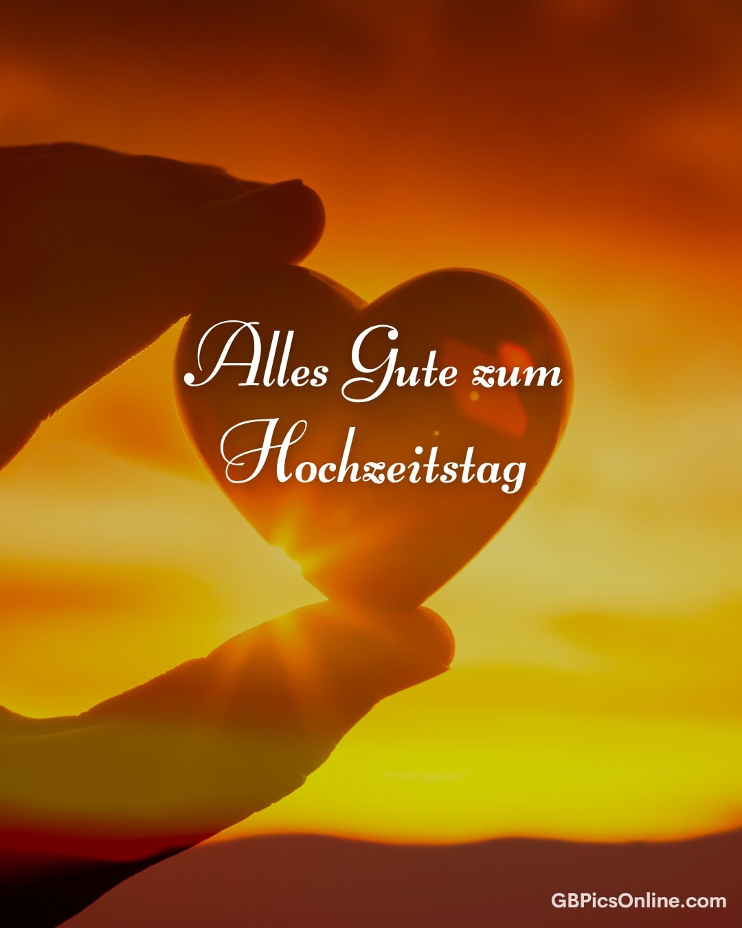 Eine Hand hält ein Herz aus Glas vor einen Sonnenuntergang, darauf steht „Alles Gute zum Hochzeitstag“