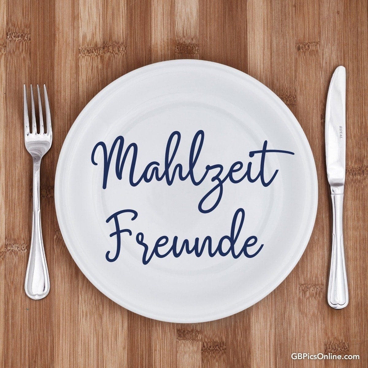 Ein leerer Teller mit der Aufschrift „Mahlzeit Freunde“ zwischen Gabel und Messer auf Holztisch