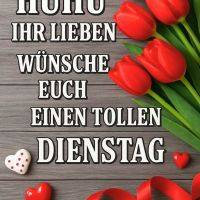 Grußtext auf Holzuntergrund mit roten Tulpen, roten Herzen und rotem Band