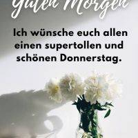 Grußtext „Guten Morgen“ über einer Vase mit weißen Blumen vor hellem Hintergrund