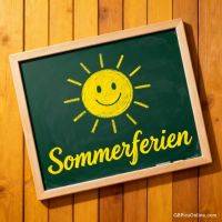 Grüne Tafel mit gemalter lächelnder Sonne und dem Wort „Sommerferien“ vor Holzbrettwand
