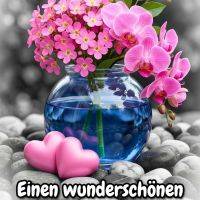 Blauer Glasvasenstrauß mit pinken Blüten und Orchideen, davor zwei rosa Herzen auf Kieseln