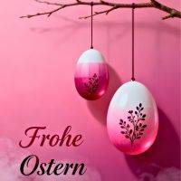 Zwei rosa-weiße Ostereier hängen an einem Zweig vor pinkem Hintergrund, mit Schriftzug „Frohe Ostern“