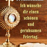 Goldene Monstranz mit Kreuz und Hostien auf einem Teller vor Holzhintergrund mit Grußtext