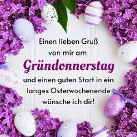 Lila Fliederkranz mit bunten Ostereiern auf weißem Holz, Gruß zum Gründonnerstag in der Mitte