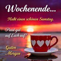 Rote Tasse mit weißen Herzen auf Untertasse am Wasser, im Hintergrund Sonnenaufgang und Wochenendgruß