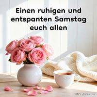 Rosa Rosen in weißer Vase neben Teetasse und Strickdecke auf hellem Holztisch