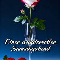 Weiße Rose mit roten Rändern in einem Sektglas, zwei rote Rosen davor, Grußtext auf blauem Hintergrund