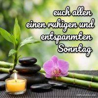Zen-Stillleben mit Bambus, Kerzenlicht, schwarzen Steinen und pinker Orchidee vor grünem Hintergrund