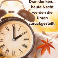 Wecker mit römischen Ziffern neben Herbstblatt, Hinweis auf Zeitumstellung und eine Stunde länger schlafen
